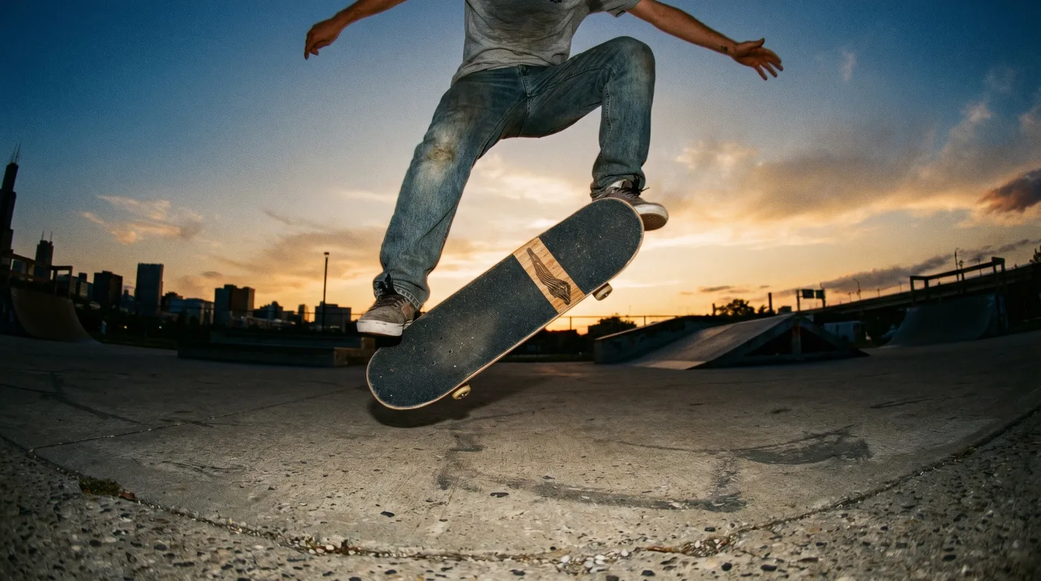 Skateboarder mid-kickflip, the board caught on its edge rotating beneath the feet against a sunset sky