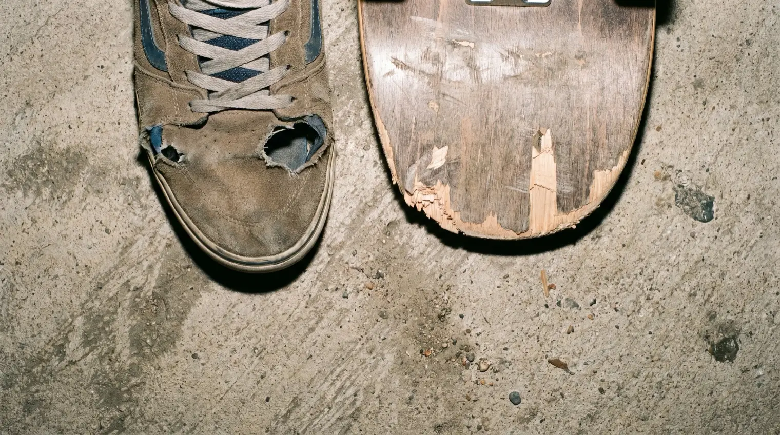 Destroyed skate shoe with an ollie hole next to a chipped skateboard tail on concrete